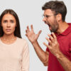 Furious bearded guy screams and gestures angrily, yells at woman, have dispute, pose together over white background. Strict boss being angry with not responsible colleague. What have you done?